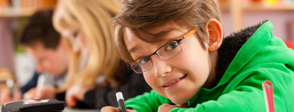 Ein Junge in grünem Pullover lehnt sich auf einen tisch und hält einen Stift in der Hand.