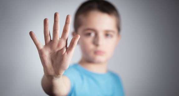 Junge im Grudschulalter zeigt mit der Hand ein Stop an 