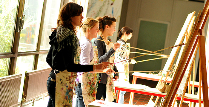 Bier Schülerinnen stehen an Staffeleien und malen mit langen Pinseln.