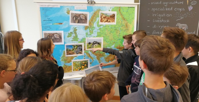 Ein Junge zeigt auf eien Landkarte Europas, um ihn herum stehene andere Kinder.