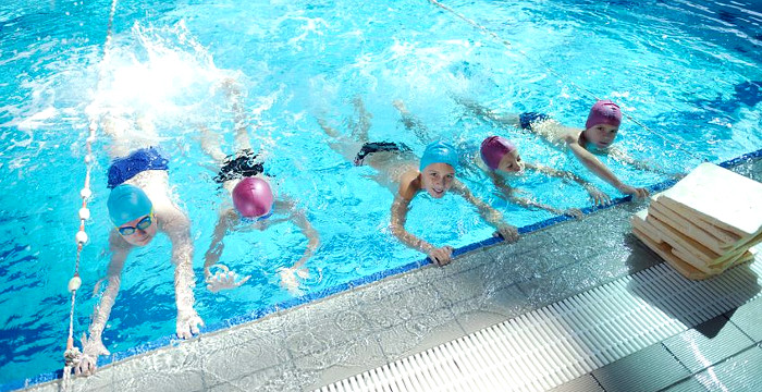 Fünf Kinder halten sich am Rand eines Schwimmbeckens fest.