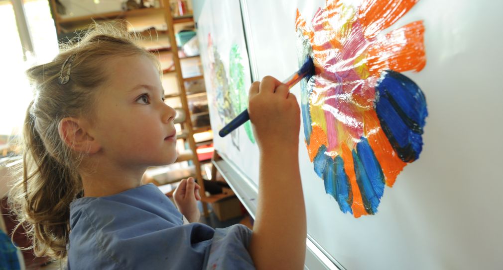 Ein Mädchen malt an eine Tafel mit bunter Farbe.