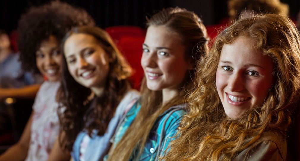 Vier Mädchen sitzen nebeneinander, im Hintergrund sind rote Theatersessel