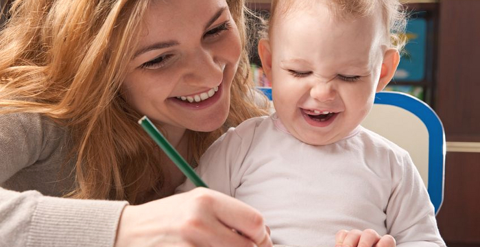 Einen Mutter malt vor ihrem Kind ein Bild, beide lachen dabei.