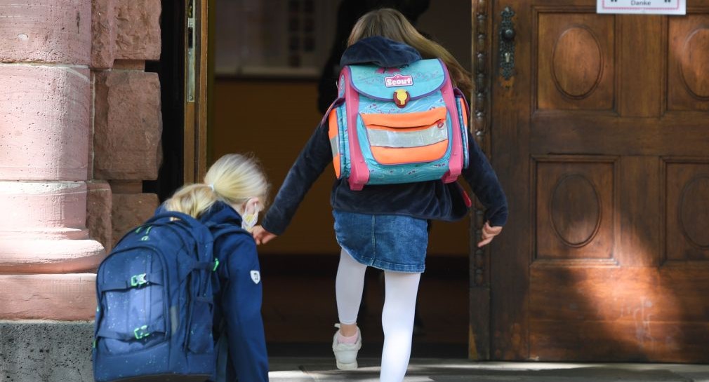 Zwei Mädchen laufen in ein Schulgebäude.