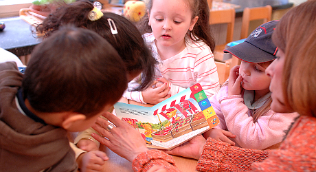 Eine Erzieherin liest in einer Krippe mehreren Kindern aus einem Buch vor. 