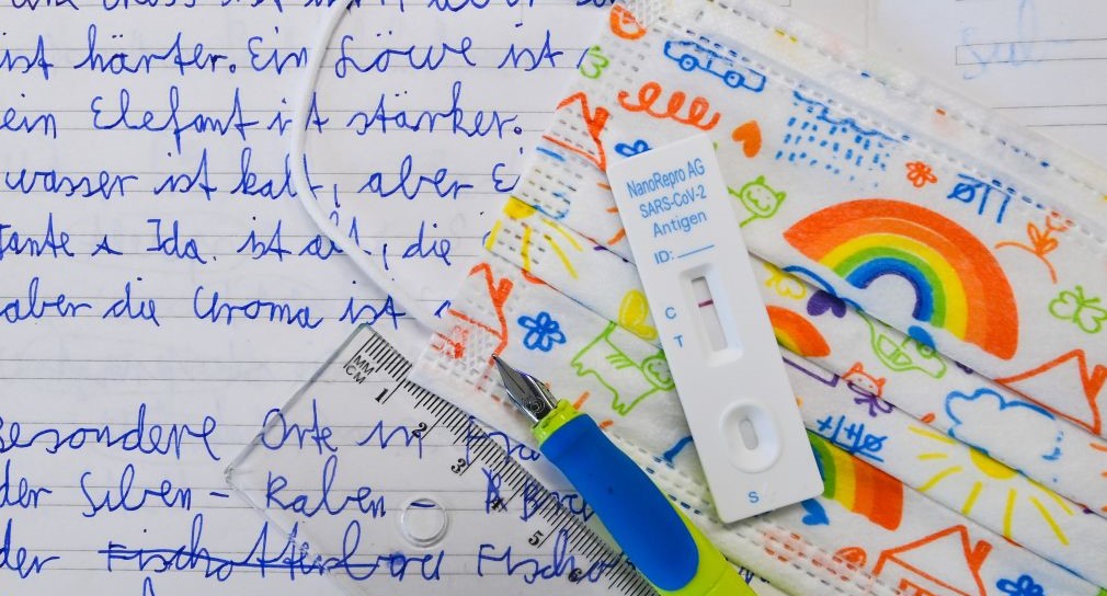 Ein Corona-Testsrteifen sowie ein Füller liegen auf einem beschrifteten Blatt Papier. und eine