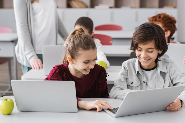 Zwei Kinder sitzen vor Laptops im Klassenzimmer