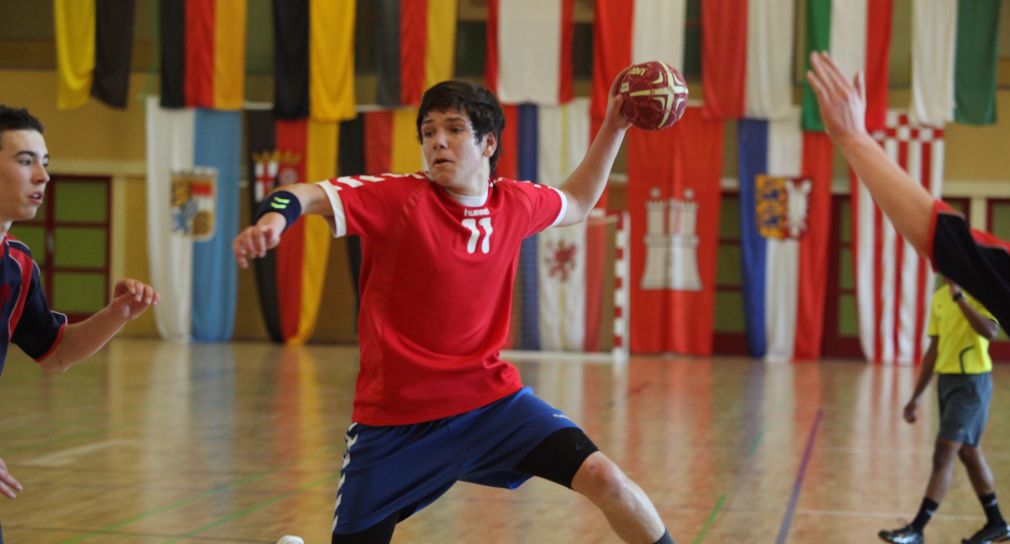 Ein Handballspieler in rotem Trikot holt zum Wurf aus.