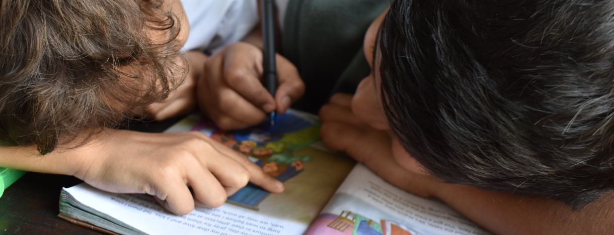 Zwei Jungen lesen ein Buch und schreiben dabei mit einem Stift hinein