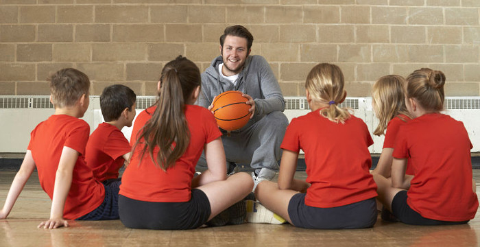 Ein Mann sitzt vor einer Reihe Mädchen in Sportkleidung, er hält einen Basketball in der Hand .
