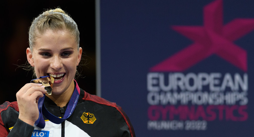 Die Turnerin Elisabeth Seitz beißt auf ihre Goldmedaille. Im Hintergrund ist das Logo der European Championships in München zu sehen.