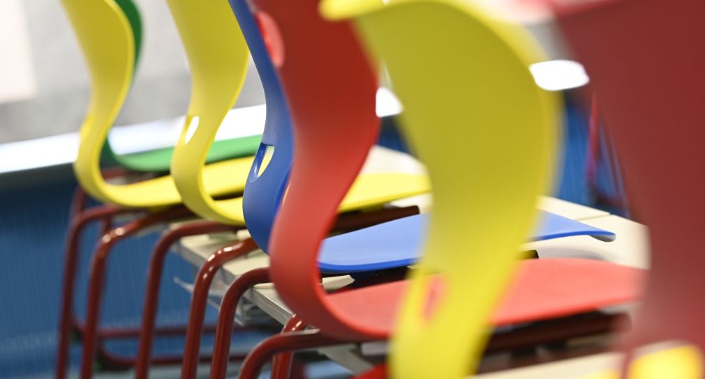 Bunte Stühle in einem Klassenzimmer sind auf den Tischen aufgestellt.