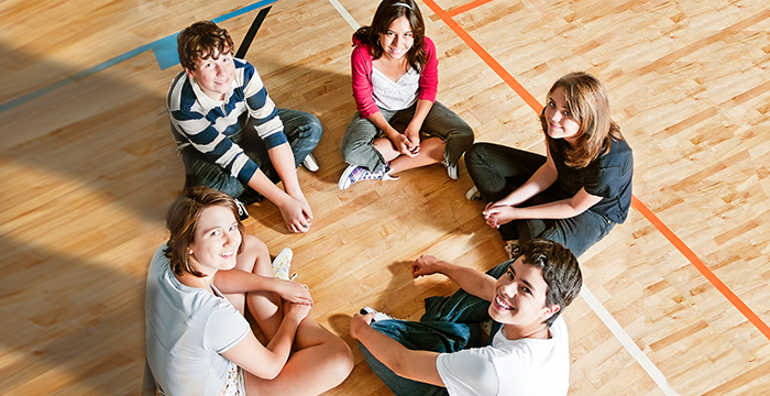 Eine Gruppe von Jungen und Mädchen sitzen in eienr Turnhalle im Kreis. 