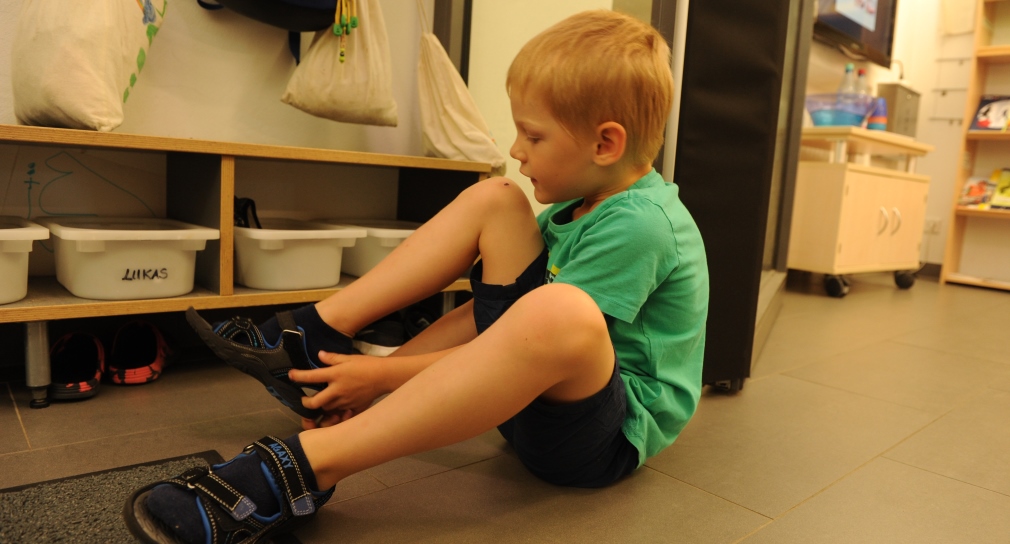 Ein kleiner Junge zieht sich seine Schuhe an. 
