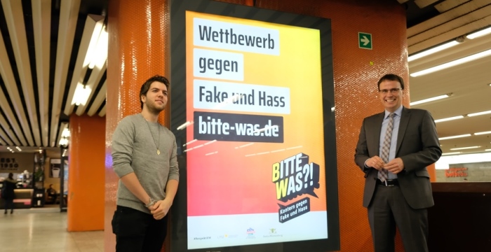 Zwei Männer stehen neben einem Plakat.
